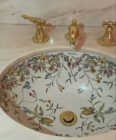 a bathroom sink decorated with flowers and gold faucets