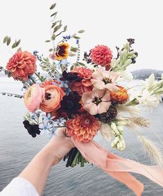 a person holding a bouquet of flowers in their hand near the water's edge