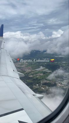 the wing of an airplane flying over a city below clouds and mountains in the distance