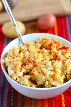 a white bowl filled with food sitting on top of a colorful table cloth next to potatoes