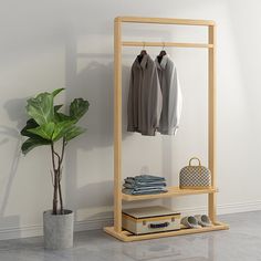 a wooden rack with clothes and shoes next to a potted plant on the floor