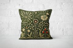 a green pillow with flowers and leaves on the front, against a white brick wall