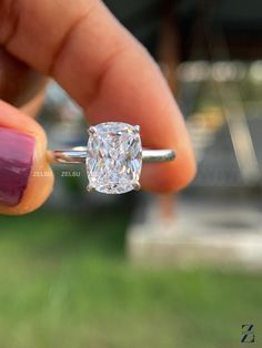 a woman's hand holding a diamond ring in front of her face with the center stone visible