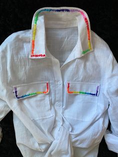 a white shirt with multicolored stripes on the chest and collar, sitting on a black surface