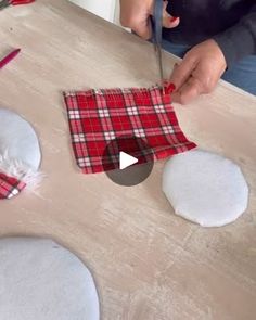 a person cutting fabric with scissors on top of a wooden table in front of another person