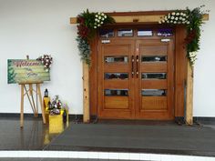 a welcome sign is in front of a large wooden door with flowers on the side