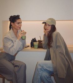 two young women sitting at a table drinking coffee and talking to each other while one looks on