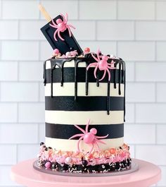 a black and white striped cake with pink sprinkles on top, topped with spider decorations