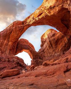 a large rock formation with a person standing under it in front of the rocks and sky