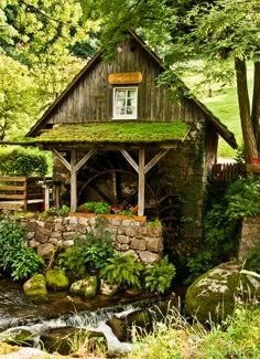 a small wooden building sitting on top of a lush green hillside next to a river