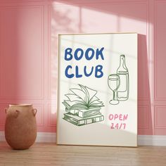 an open book club sign next to a vase with a wine bottle on it in front of a pink wall