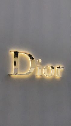 the word dior is illuminated in gold on a gray wall with a white dot