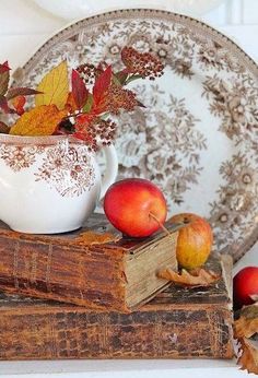 an old book with fall leaves and apples on it next to a vase filled with autumn leaves