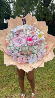 a woman standing in the grass holding a bunch of baby items on top of it