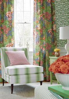 a living room with green and pink curtains, a white chair and a table in front of a window