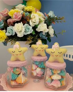 three little star cookies in glass jars on a table with flowers and balloons behind them