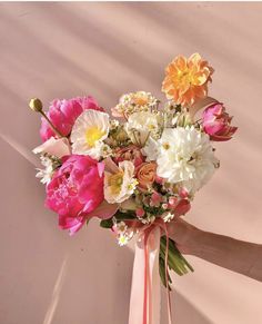 a bouquet of flowers is being held up by someone's hand in front of a wall