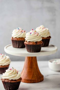 cupcakes with white frosting and sprinkles on a cake stand