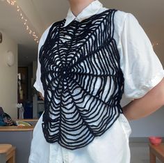 a woman wearing a white shirt and black crochet scarf over her shoulders, standing in front of a table