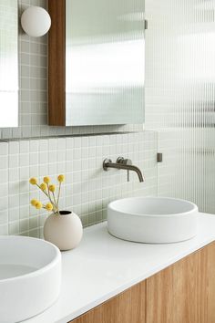 two white sinks sitting under a mirror next to a vase with yellow flowers in it