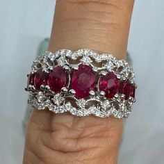 a woman's hand holding a ring with three ruby stones in the middle and two white diamonds on each band