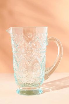 a clear glass pitcher sitting on top of a white table next to a brown wall