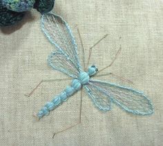 a blue dragonfly sitting on top of a piece of cloth next to a crocheted stuffed animal