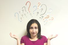 a woman is standing in front of a white wall with question marks above her head