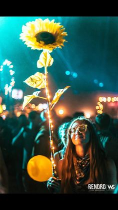 a woman standing in front of a crowd holding a sunflower with lights on it