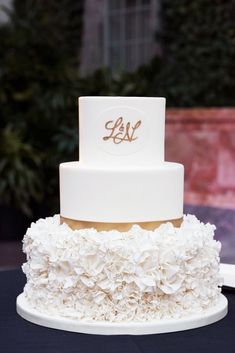 a three tiered white and gold wedding cake with ruffles on the bottom