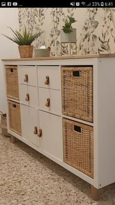 a white dresser with wicker drawers and baskets on the top shelf, in front of a wallpapered wall