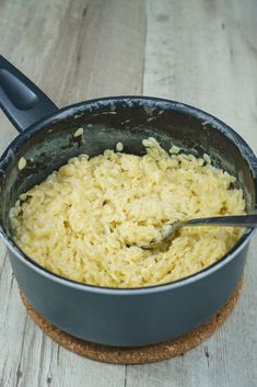 a pot filled with yellow rice on top of a wooden table next to a spoon