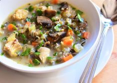 a bowl of soup with mushrooms, carrots and parsley on the side next to a fork