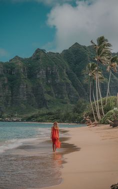 a woman standing on top of a sandy beach next to the ocean with mountains in the background