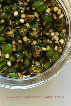 some green peppers are in a glass bowl on a white counter top with peanuts and garlic