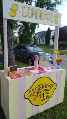 a lemonade stand is set up in the grass near a tree and parked car