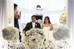 a bride and groom sitting on a couch in front of a table with white flowers