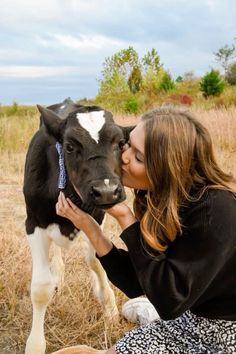 a woman kissing a black and white cow on the nose while sitting in a field