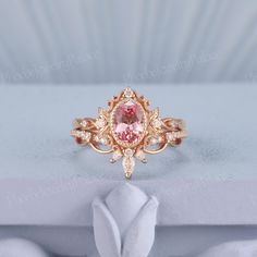 a pink diamond ring sitting on top of a white flower shaped object with diamonds around it