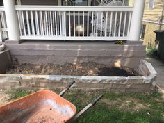 an orange wheelbarrow sitting in front of a house with dirt on the ground