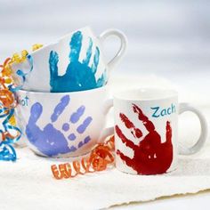 two coffee mugs with hand prints painted on them, sitting next to each other