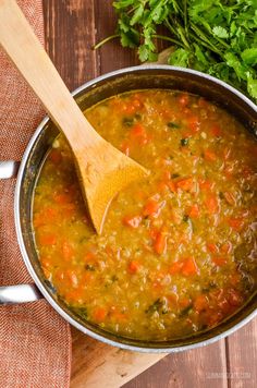 a wooden spoon in a pot filled with soup and garnished with parsley