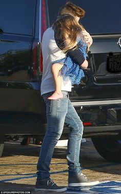 a woman holding a baby in her arms while walking past a black suv with the door open