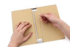 two hands holding an open binder on top of a piece of brown paper next to each other