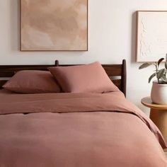 a bed with pink sheets and pillows next to a painting on the wall above it