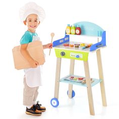 a young boy holding a cardboard box and standing next to a toy stove with food on it