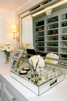 a white vanity with flowers and candles on the counter in front of a large mirror