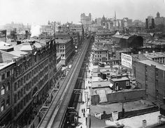 an old black and white photo of a train on tracks in the middle of a city