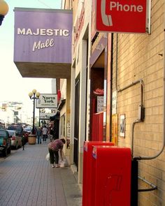 a red phone booth sitting on the side of a building next to a sidewalk with people walking by