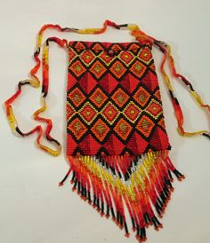 This is a exquisitely crafted beaded bag in a vibrant red, orange, black, gold and yellow beads creating a stunning geometric design.   Perfect size to hold cell phones.  This is a perfect gift as it is, or you can tuck something else inside. It has a flap and bead closure.  It measures 7 inches long with a 3 1/2 inch tapered fringe.  It measures 4 1/4 inches wide. It's got a long beautifully beaded handle that measures a 22 inch drop that can be worn cross body or over the shoulder.  It weighs Beaded Rectangular Shoulder Bag For Festivals, Red Bohemian Beaded Shoulder Bag, Bohemian Red Beaded Shoulder Bag, Red Rectangular Shoulder Bag For Festivals, Traditional Red Beaded Bags, Handmade Multicolor Phone Bag For Gift, Multicolor Rectangular Beaded Necklaces, Red Beaded Rectangular Shoulder Bag, Traditional Beaded Rectangular Shoulder Bag